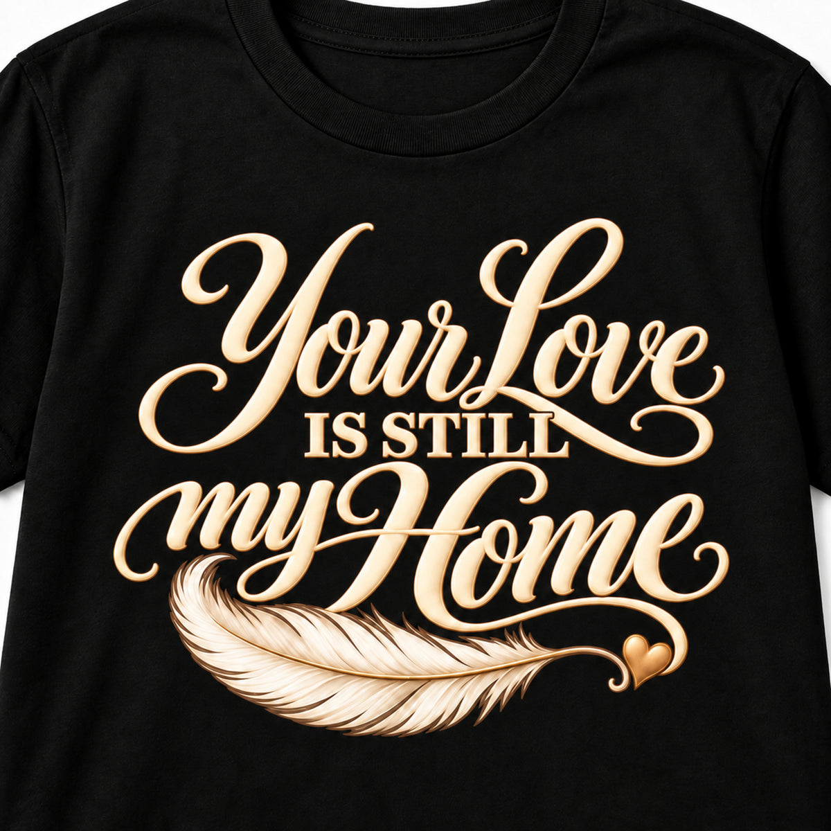 Closeup of the cream lettering, feather and golden heart on the Your Love Is Still My Home T-shirt