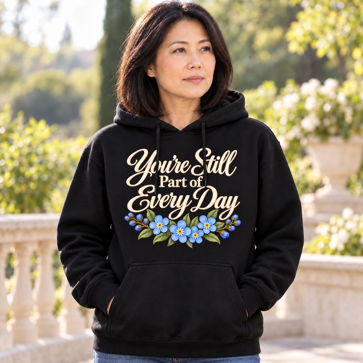 Woman wearing the black You're Still Part of Every Day hoodie on a quiet garden terrace